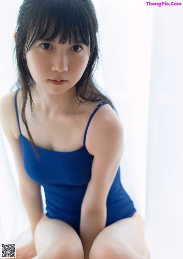 A woman in a blue bathing suit sitting on a bed.
