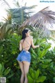 A woman in a black top and denim shorts standing in front of a palm tree.