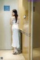 A woman in a white dress standing in an elevator.