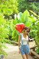 A woman holding a red heart shaped balloon on a wooden bridge.