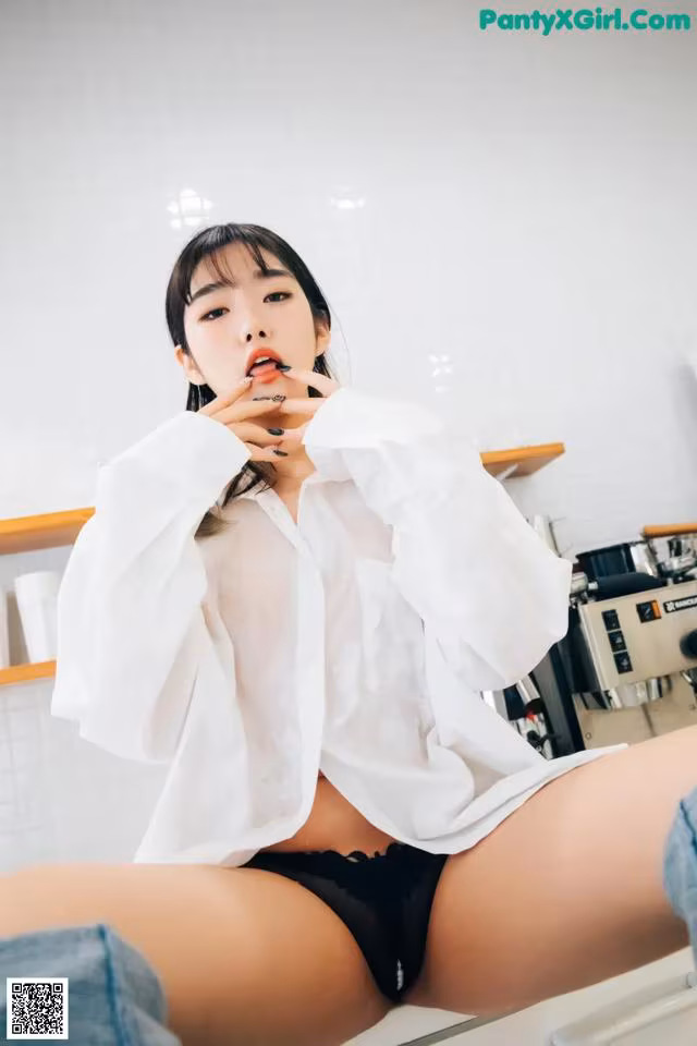 a woman in a white shirt and black panties sitting on a counter