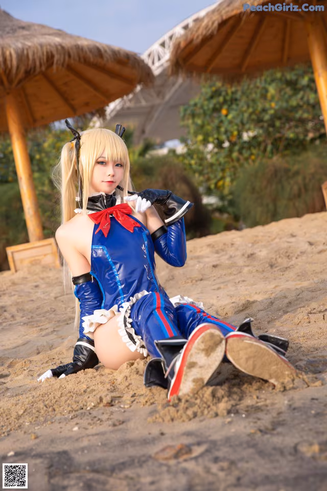 A woman in a blue and red outfit sitting on the sand.