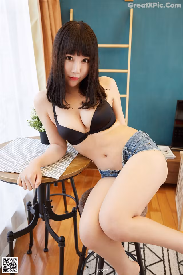 A woman in a black bra and denim shorts sitting at a table.