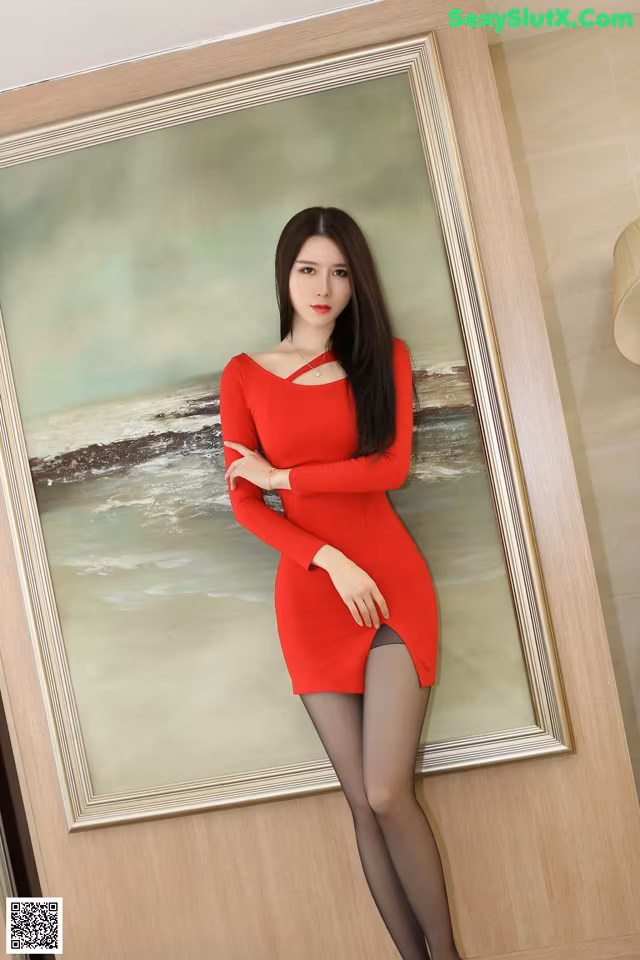 A woman in a red dress posing in front of a painting.