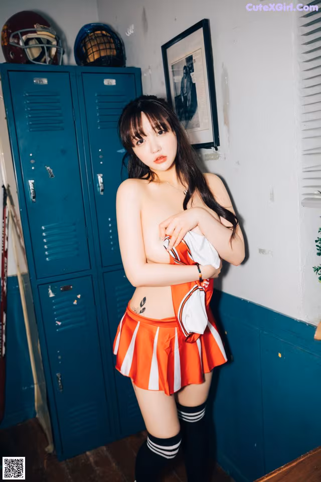 A woman in a cheerleader outfit posing in front of lockers.
