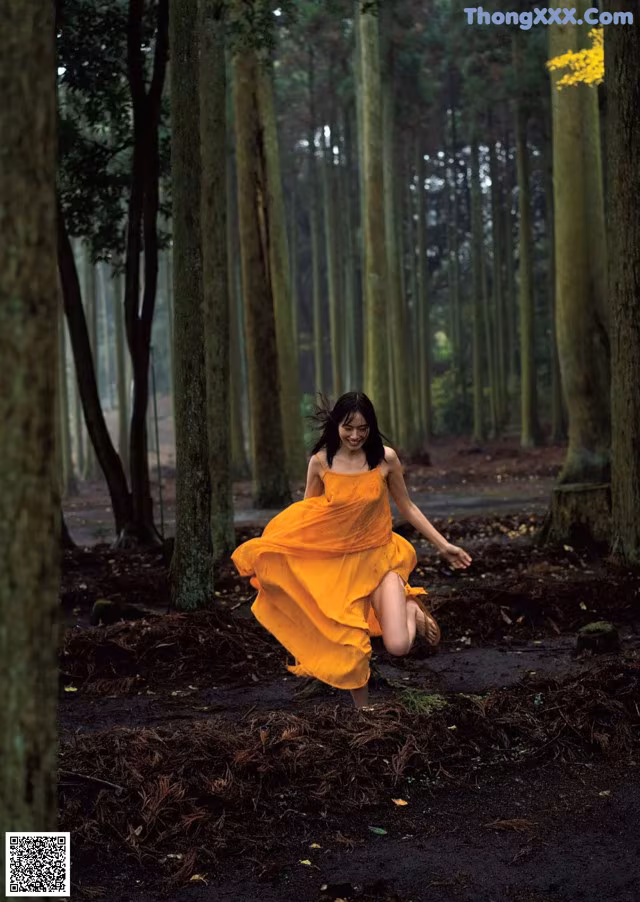 A woman in a yellow dress running through a forest.