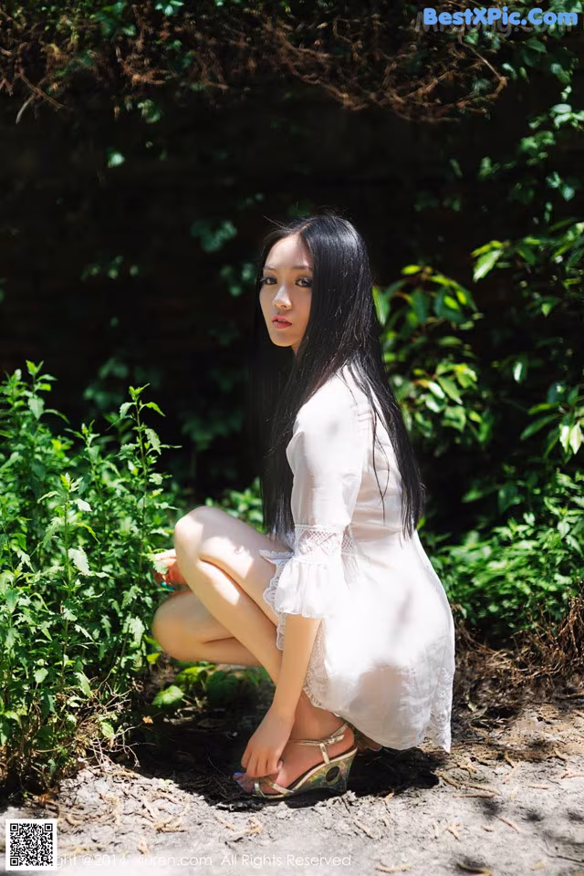 A woman in a white dress crouching down in the woods.