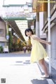 A woman in a yellow dress leaning against a pole.