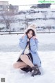 A woman sitting in the snow wearing a blue coat and hat.