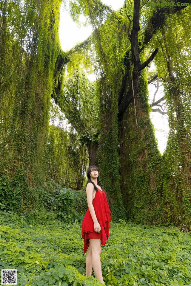 A woman in a red dress standing in the middle of a forest.