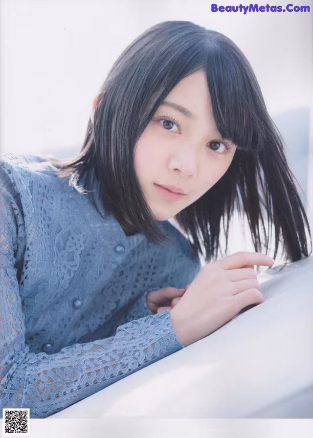 A woman with long black hair leaning against a wall.