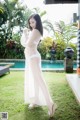 A woman in a sheer white dress standing by a pool.