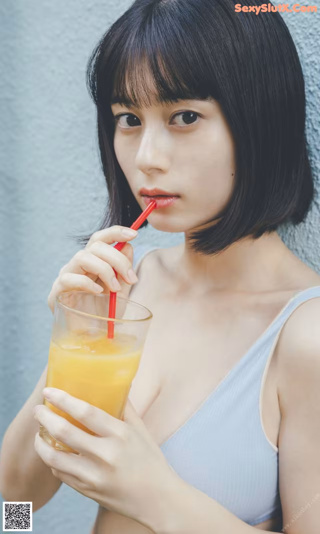 A woman holding a glass of orange juice with a straw.