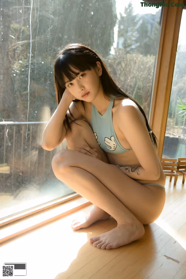 A woman in a blue bikini sitting on a window sill.