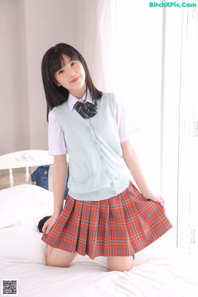 A young woman in a school uniform posing on a bed.