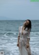 A woman in a sheer white dress standing on the beach.