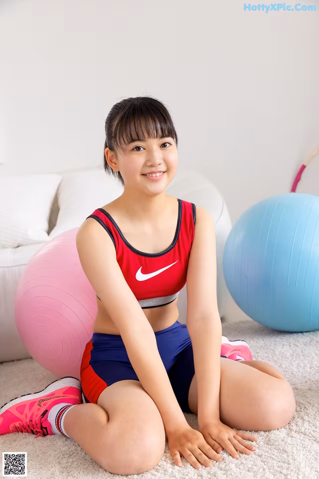 A young woman sitting on the floor next to two exercise balls.